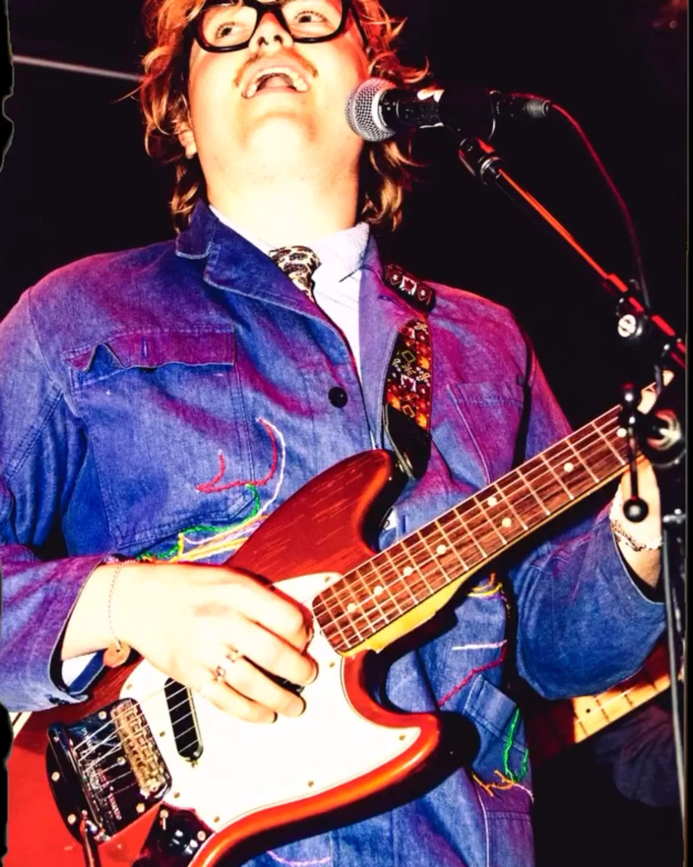 Closeup of a man standing behind a microphone with a red electric guitar in his hands