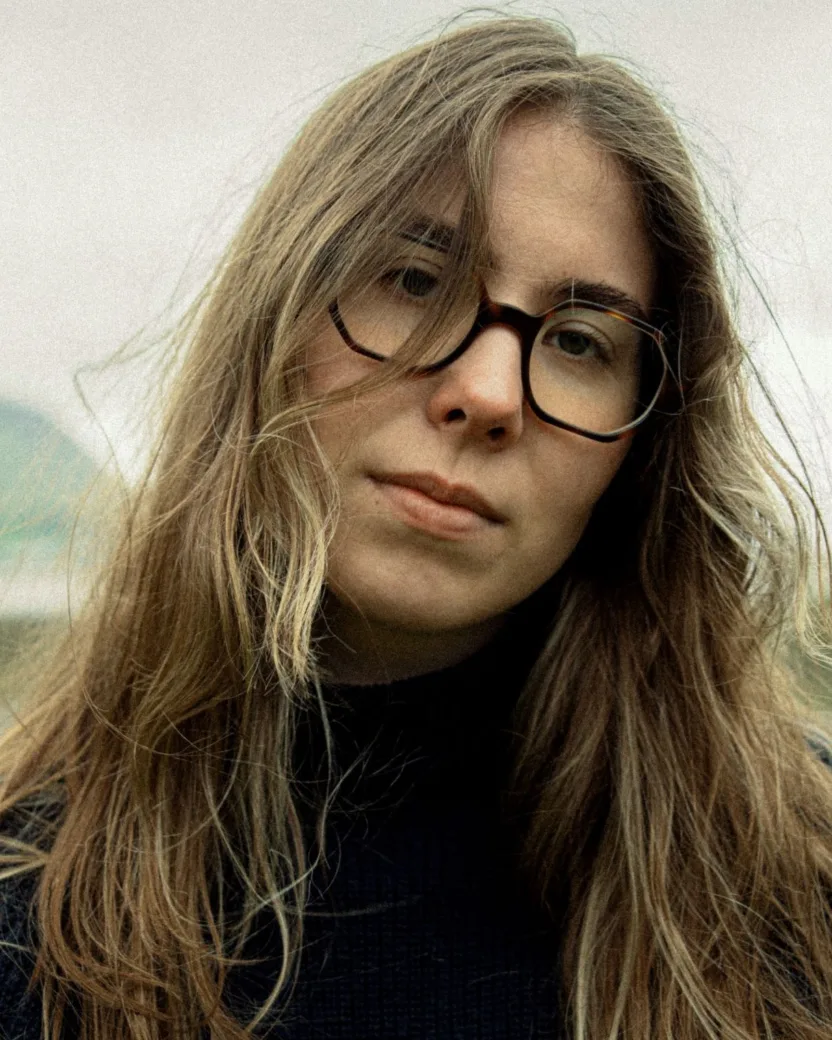 Long haired woman with rectangular glasses with her head tilted slightly to the right and some of her hair slightly falling over her eyes